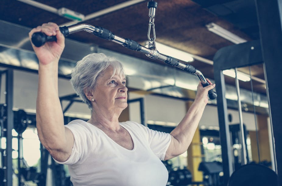 An older woman uses an exercise machine to train her arm muscles.