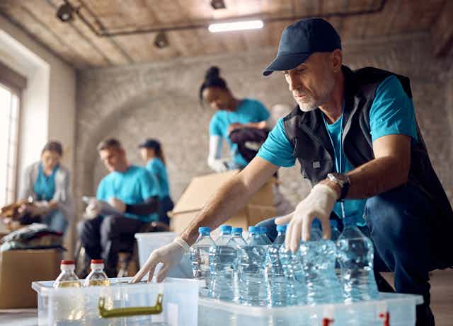 Man sorting bottled water and other aid in a room with other volunteers.