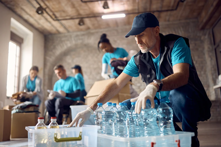 Man sorting bottled water and other aid in a room with other volunteers.