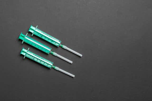 Three green syringes on a black background.