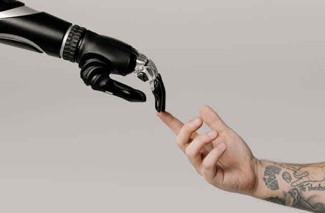 Mão robótica toca com os dedos uma mão humana