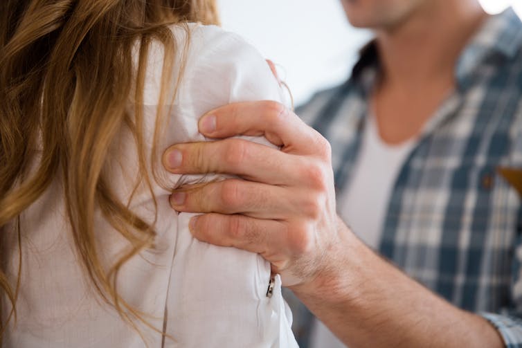 Close up of a man aggressively placing his hand on a woman's arm.