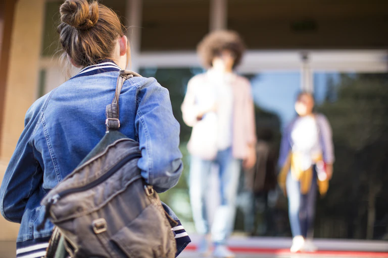 A young woman carrying a backpack walks into a building