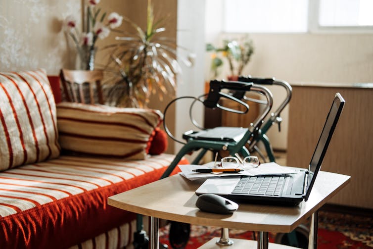 A walker stands beside a table with a laptop and paperwork on it in a living room