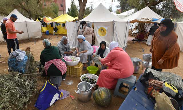 Women wearing hijab cook outside tents.