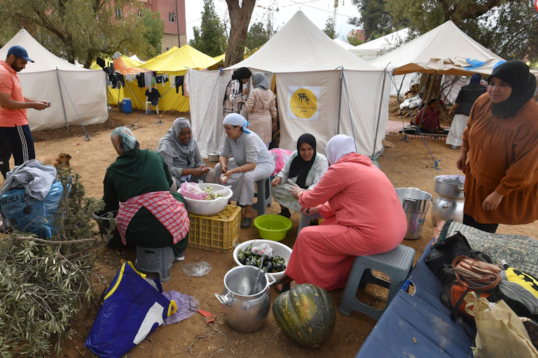 Women wearing hijab cook outside tents.