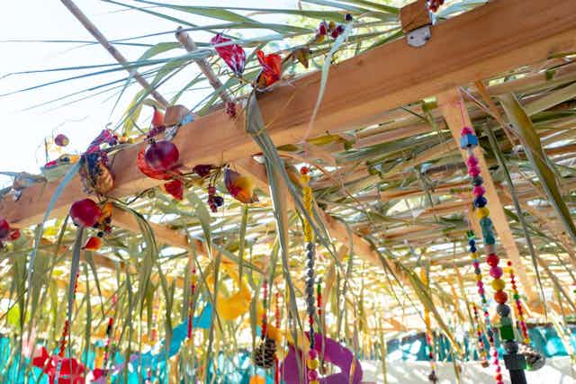 The roof of a structure built out of palm fronds, wood beans, and brightly colored decorations.