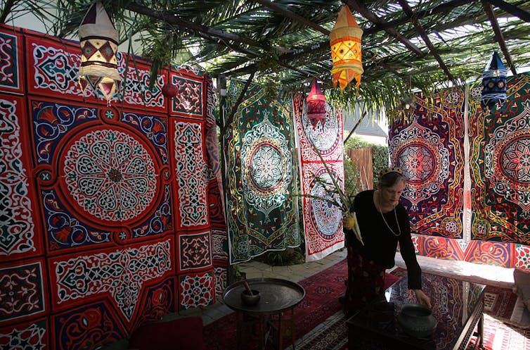 A woman in black arranges items in a hut with large, colorful abstract designs on the sides.
