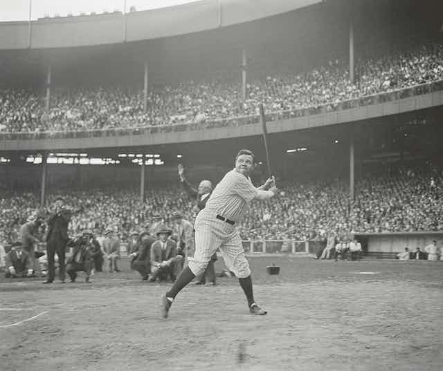 A black and white photo of Babe Ruth in uniform, holding his bat, about ready to hit, as scores of fans look on.