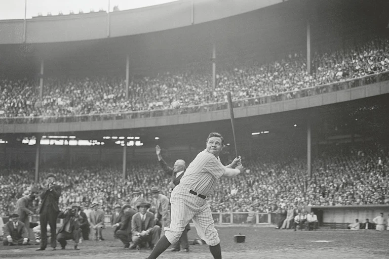 A black and white photo of Babe Ruth in uniform, holding his bat, about ready to hit, as scores of fans look on.