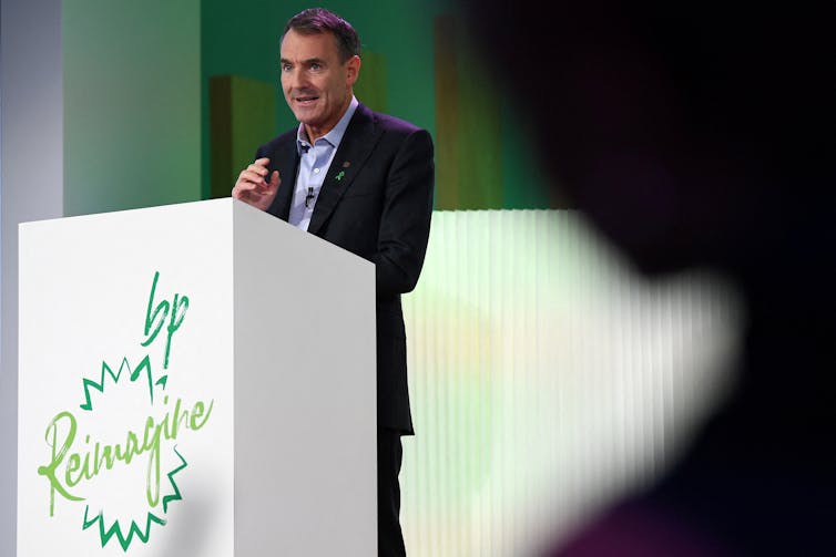 Bernard Looney, in a suit, stands at a podium with the word 'Reimagine BP' on the front.