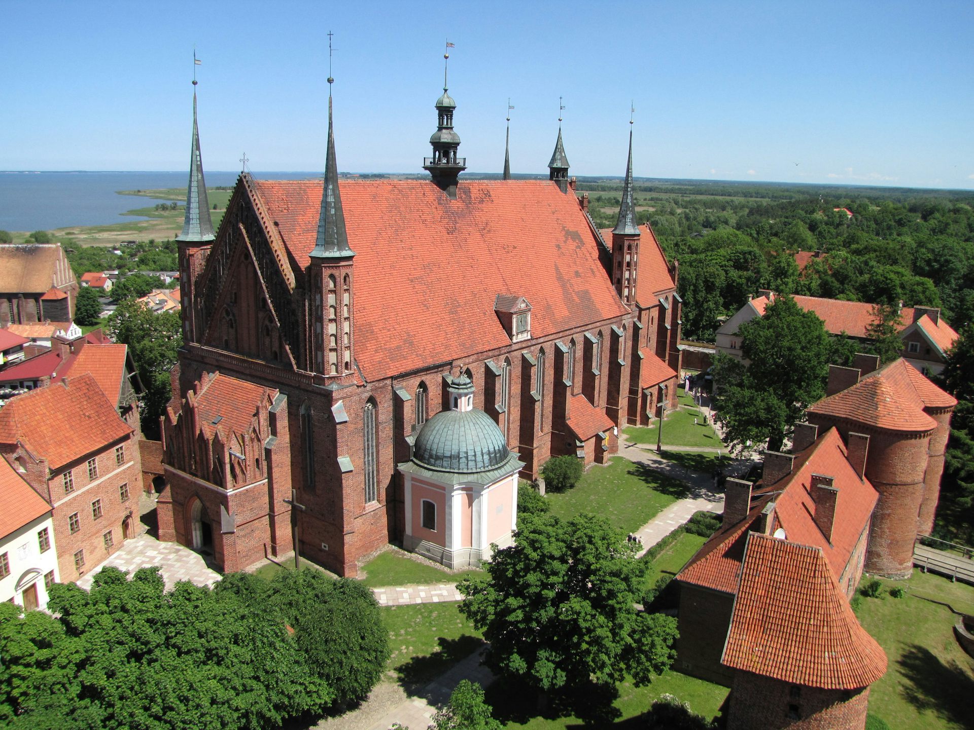 A big brick church with narrow towering steeples in center and at corners, and a red roof.