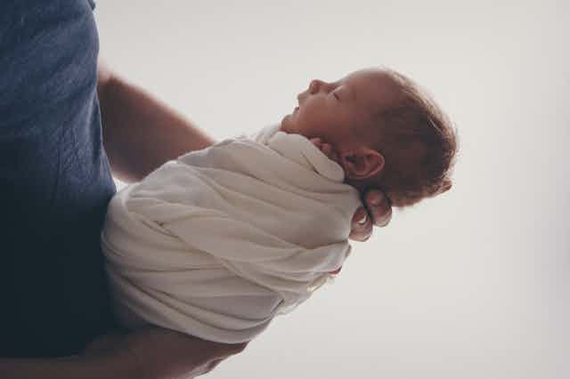 Photo d’un nouveau-né dans les bras d’un adulte.
