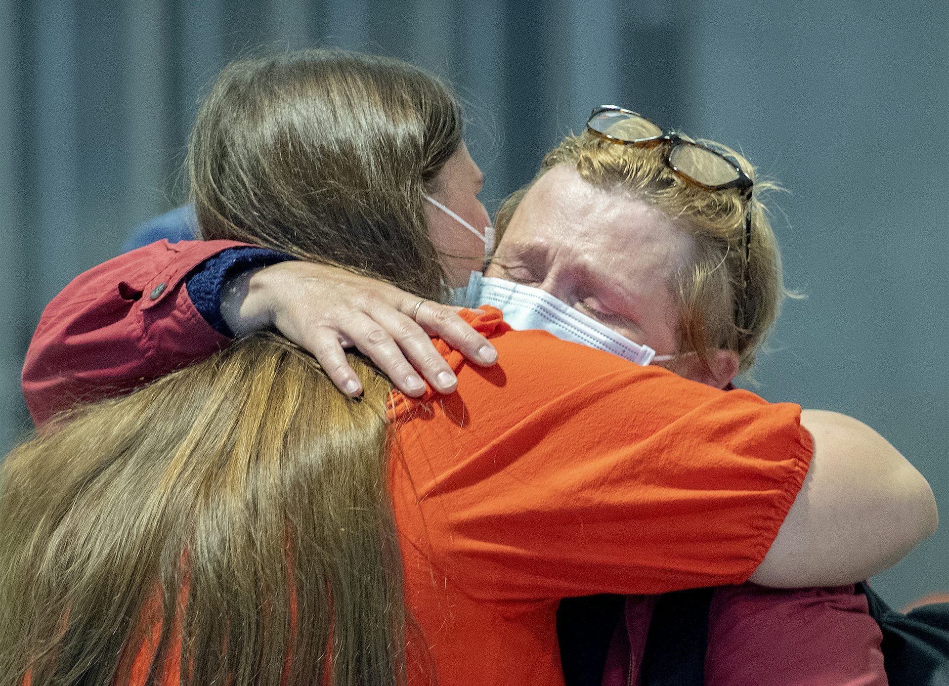 A blonde woman wearing a mask cries as she's embraced by a woman with long dark blonde hair.