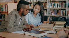 Young African American and Asian college students work together at a library.