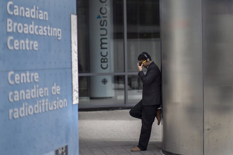 A man with his hand on his head leans against a wall outside the CBC building.