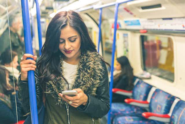 A young woman looks down at her mobile phone while standing on a London underground train