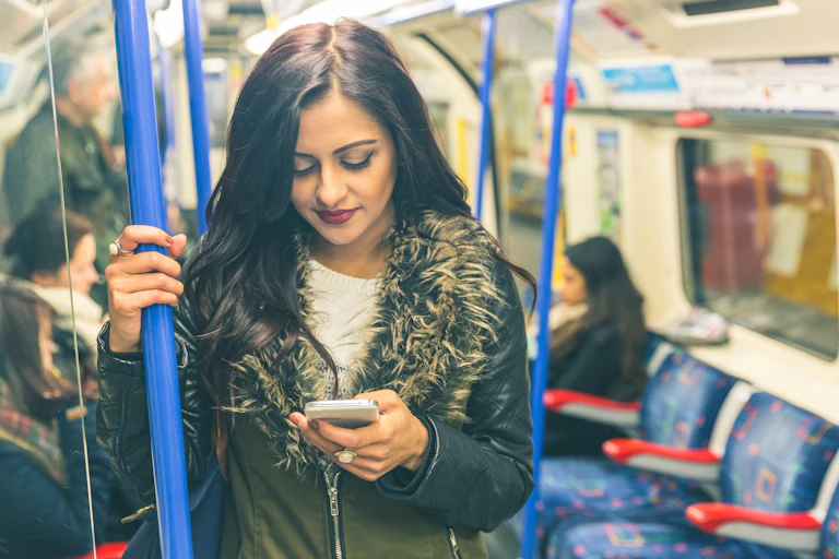 A young woman looks down at her mobile phone while standing on a London underground train