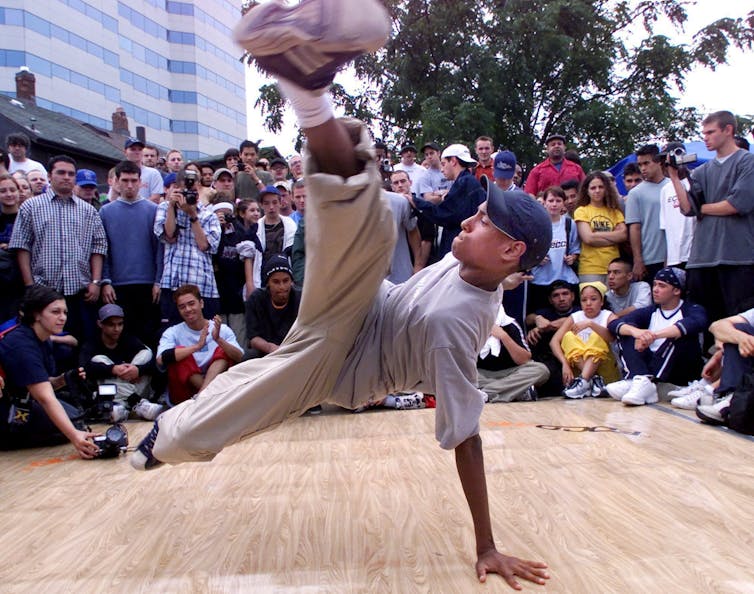 A person seen breakdancing surrounded by people watching.