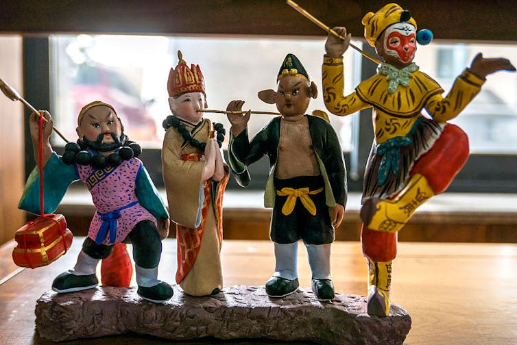 Four small, brightly painted clay figurines of people and animals in clothing.