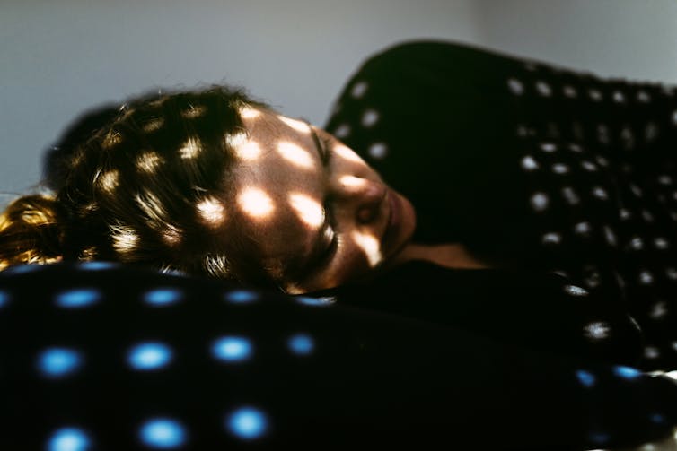 Person lying in bed, light speckled over their face.