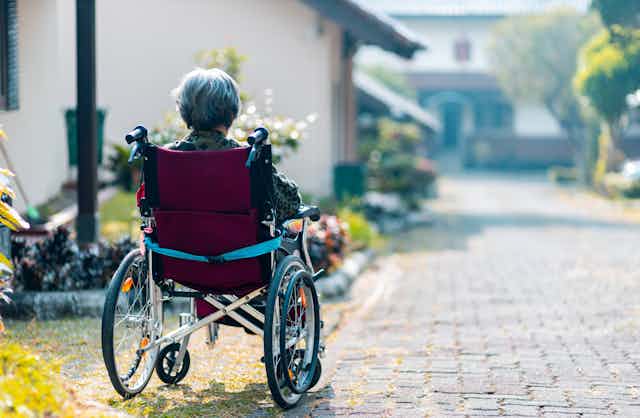 Pessoa idosa, de costas, sentada numa cadeira de rodas