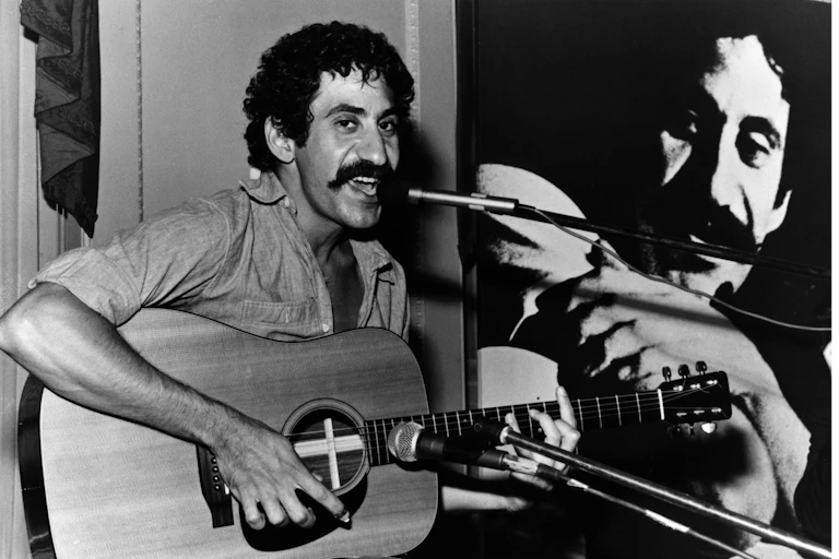 black-and-white photo of a man with curly hair and a mustache singing into a microphone