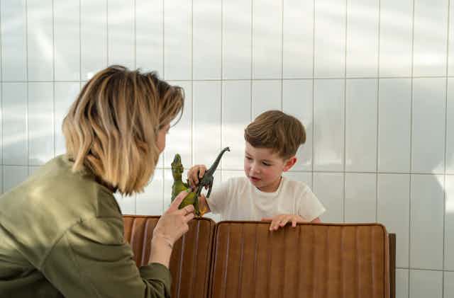 A woman and small child play with toy dinosaurs over the back of a couch.