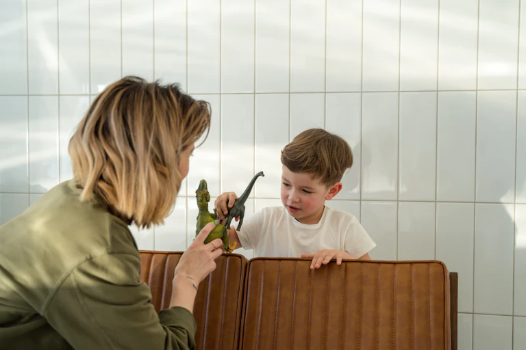 A woman and small child play with toy dinosaurs over the back of a couch.