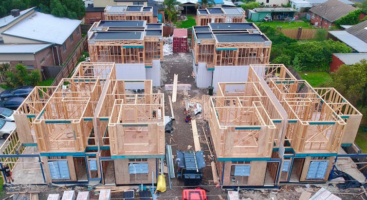 Building frames of houses are seen against an urban background.