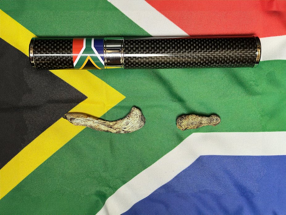 A black and silver tube, with a small South African flag on the side, and two bones lie against a large South African flag