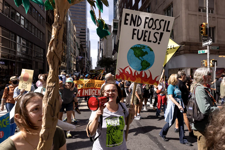 A crowd in New York City holding signs. One reads 'End fossil fuels!'