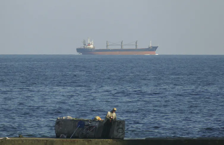 A grain cargo ship on the horison on its way to Odesa in Ukraine to pick up grain for export. In the foreground is a smaller boat.
