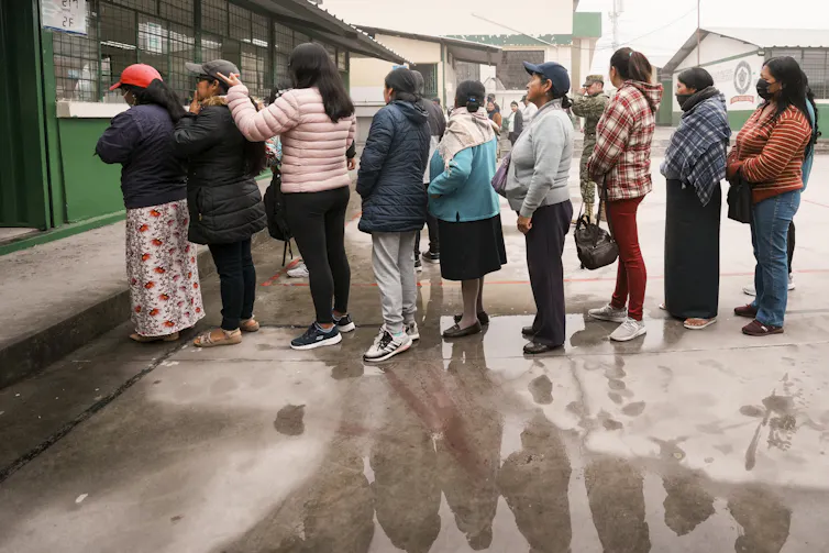 Une rangée de personnes attendent en fil pour voter, sous la pluie