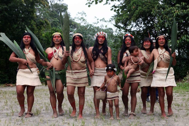 A group of Indigenous women and a child stand in a forest clearing.