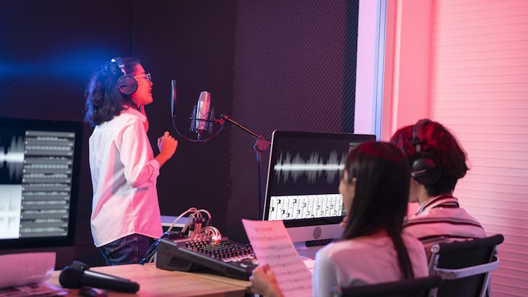 Student singer and music producer record a song in professional music recording studio.