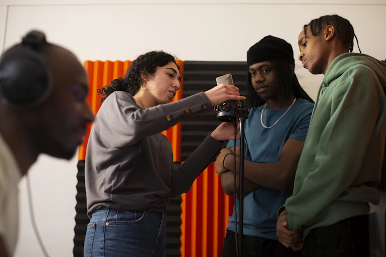 Woman adjusting microphone while rappers stand in studio.