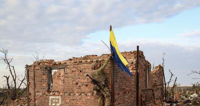 A Ukrainian soldier hoists the national flag over the remains of a house in Andriivka.