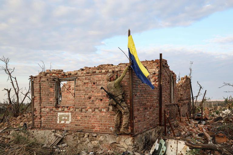 A Ukrainian soldier hoists the national flag over the remains of a house in Andriivka.