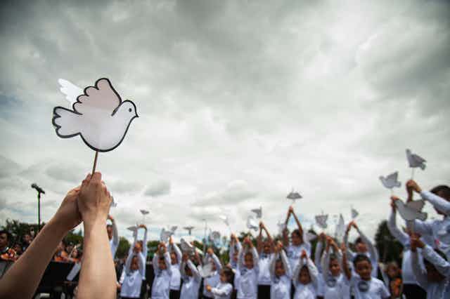 People hold little paper white doves and stand against a grey sky. 