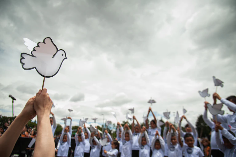 People hold little paper white doves and stand against a grey sky.