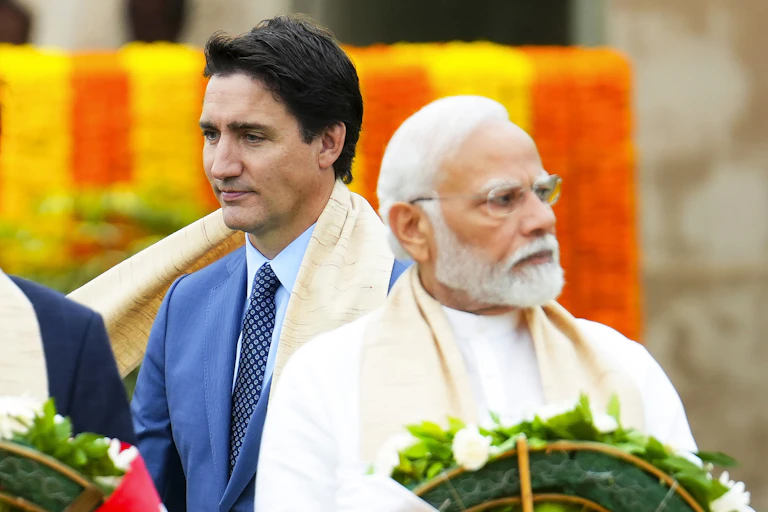 Two men, one dark-haired and an older grey-haired man, look in opposite directions.