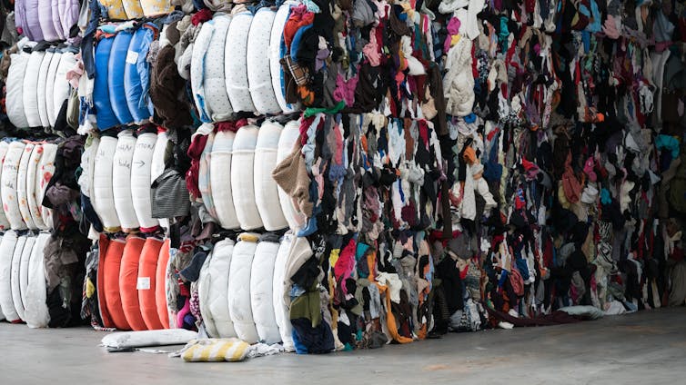 Bales of clothes stacked in piles in a warehouse.