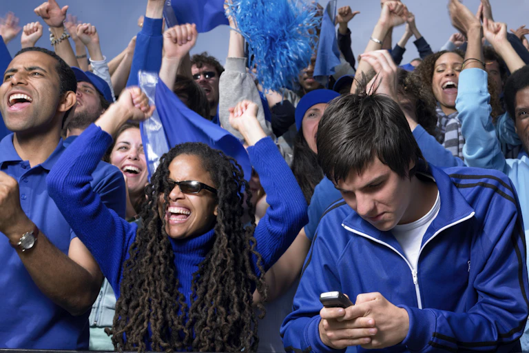 Stadium crowd cheering, one man looking at mobile phone.