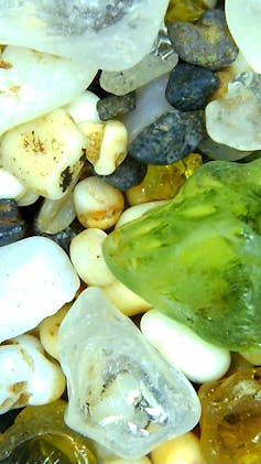 A close up image of sand, which looks like small rocks, with a green, translucent piece of sea glass