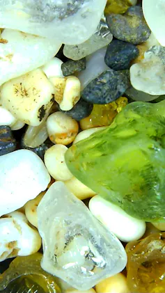 A close up image of sand, which looks like small rocks, with a green, translucent piece of sea glass
