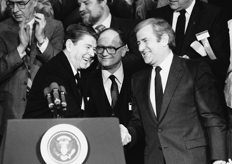 Three men in suits and ties at a lectern.