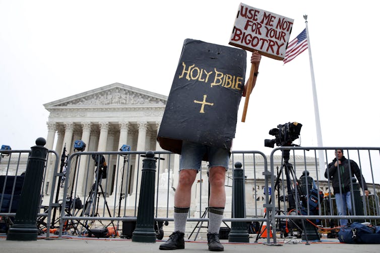 A man wears a costume of the Bible and a sign saying
