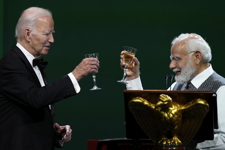 Two older grey-haired men clink their champagne glasses in a toast.