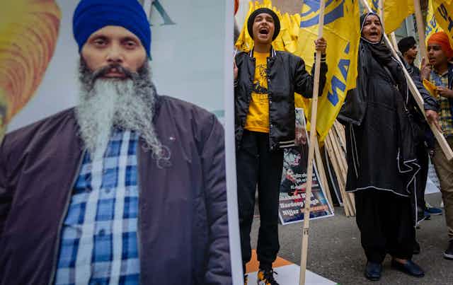 People at a protest chant and carry a large photo of a Sikh man wearing a turban